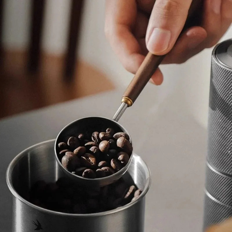 Stainless steel 25ml coffee scoop with wooden handle for precise measurements.