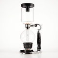 Yama Glass tabletop siphon coffee maker on a clean white background with warm studio lighting and a subtle shadow